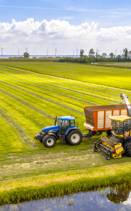 Tractor and harvester on fresh mowed green agricultural grassland under cloudy summer sky. These kind of humid meadows are very common in the Netherlands and ideal circumstances for the dairy industry.